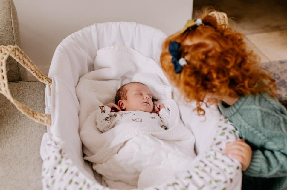 Newborn baby is sleeping and her big sister is looking at her. Newborn photo shoot in Berkshire. Newborn photographer in Hampshire Ewa Jones Photography.