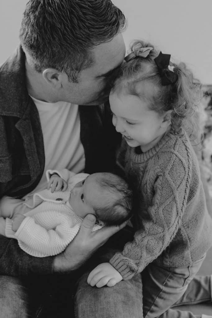 dad is cuddling both his girls. newborn photo shoot in Berkshire. Ewa Jones Photography