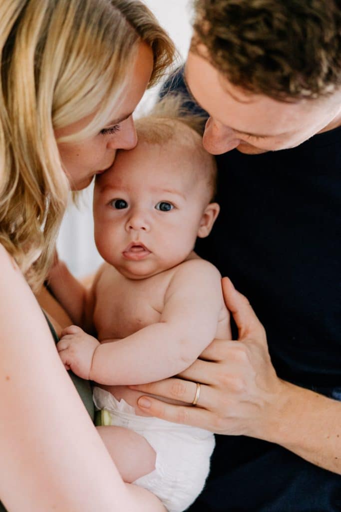 mum and dad are cuddling and kissing their baby boy. Lovely natural lifestyle photo session in Hampshire. Newborn photo shoot in Hampshire. Ewa Jones Photography