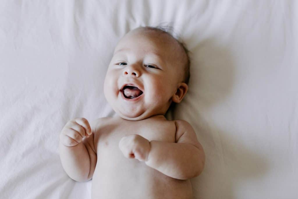 baby boy is laying on bed and smiling to the camera. Newborn photoshoot in Hampshire. Basingstoke newborn photographer. Ewa Jones Photography