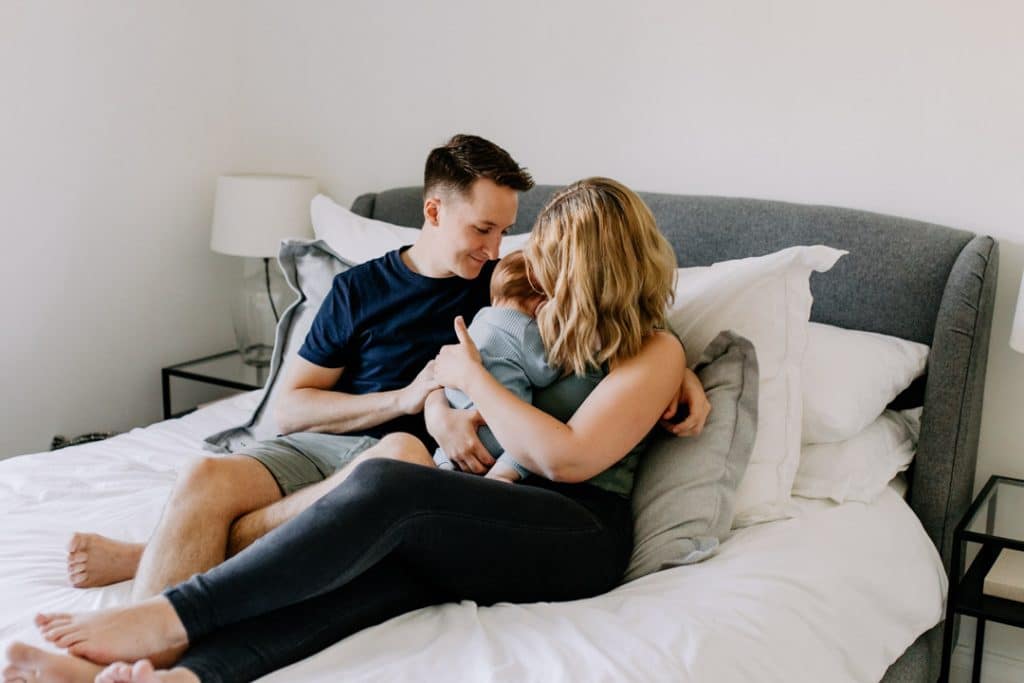 family of three is cuddling close on the bed. lovely natural lifestyle family photo session. Hampshire newborn photographer. Ewa Jones Photography