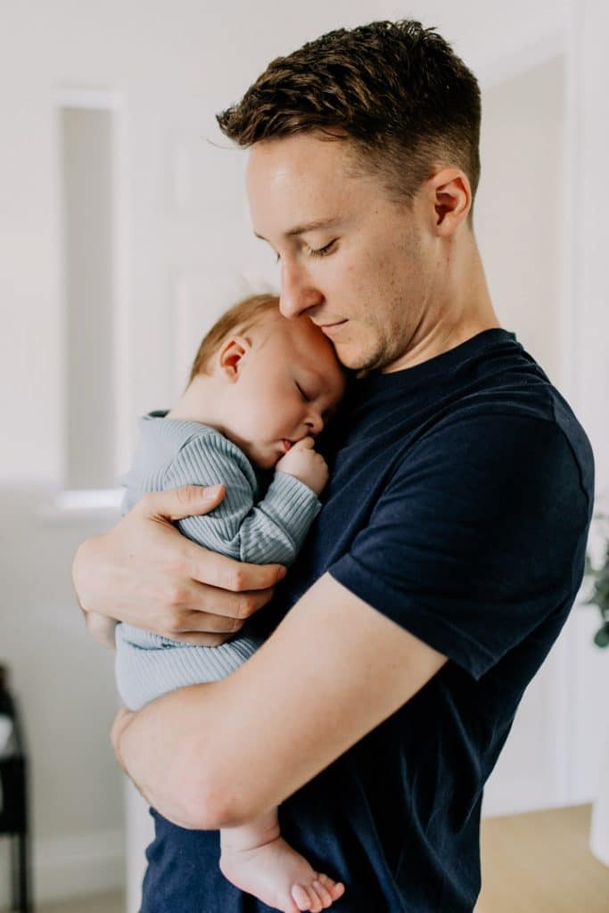 Dad is cuddling his baby boy who is sleeping. Newborn poses ideas. Lifestlye photo shoot. Hampshire newborn photographer. Ewa Jones Photography