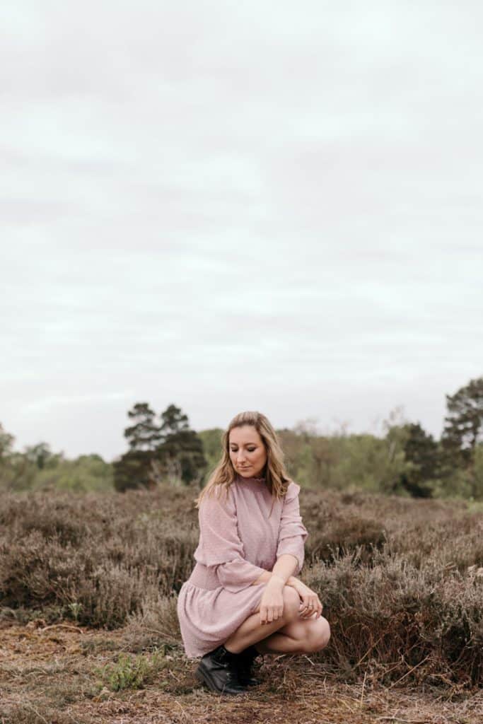 female is in the nature and looking down on the ground. she is wearing lovely pink dress. natural lifestyle female photo session in Hampshire. Hampshire photographer. Ewa jones photography