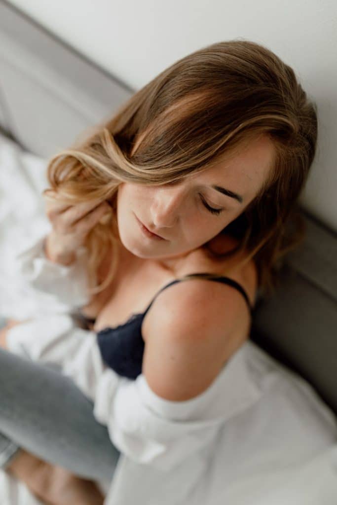 female is sitting on the bed and looking down. she is wearing white shirt and black bra. Empowering female photo sessions. Female intimate boudoir session in Basingstoke hamsphire. Hampshire photographer. Basingstoke female photographer.Ewa Jones Photography