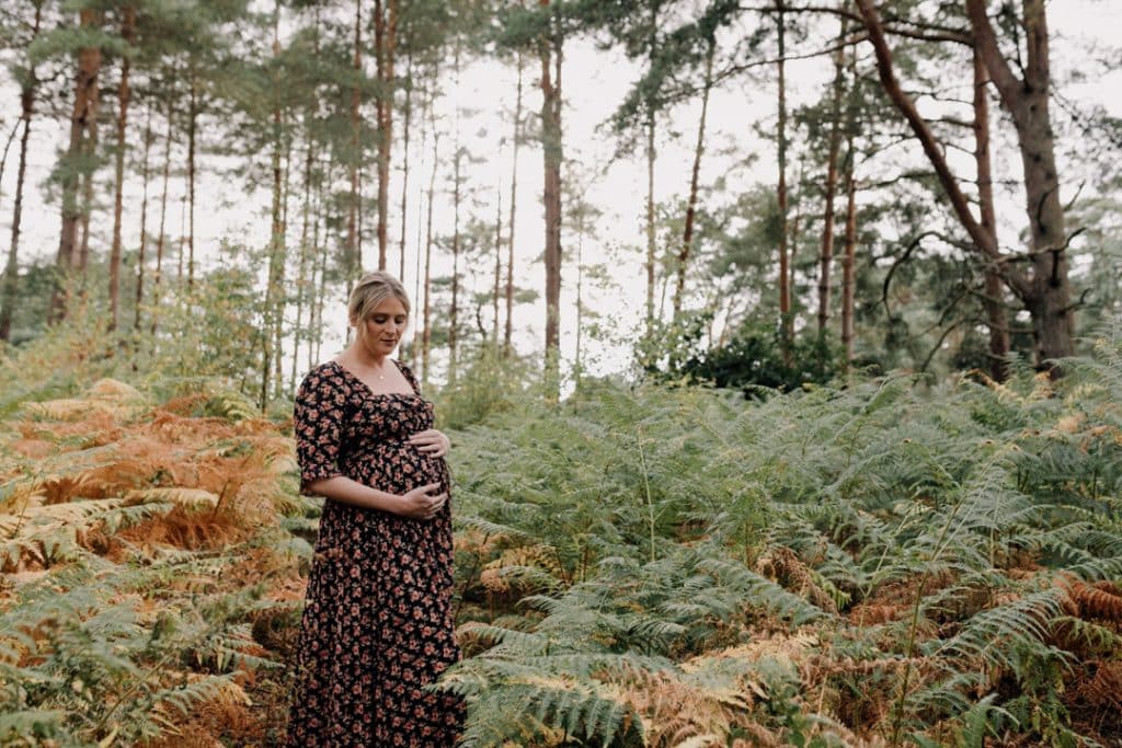 Expecting mum is standing in the forest and looking down at her baby bump. Maternity photo shoot in Hampshire. Hampshire maternity photographer. Ewa Jones Photography