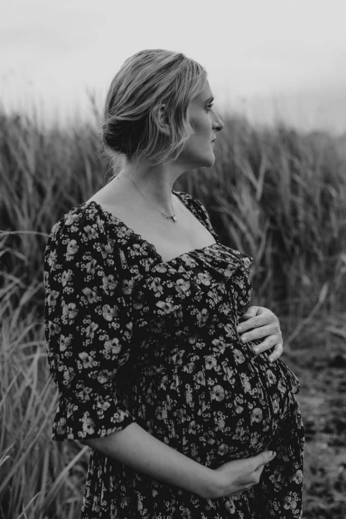 Pregnant mum is holding her bump. She is wearing lovely flower dress. Maternity photo session in Hampshire. Ewa Jones Photography