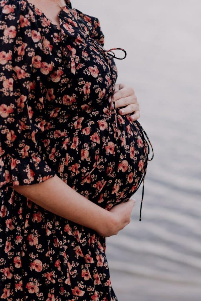 Pregnant mum is holding her bump. She is wearing lovely flower dress. Maternity photo session in Hampshire. Ewa Jones Photography