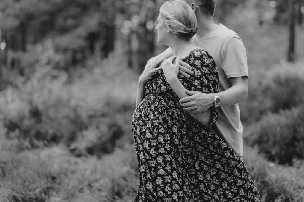 Black and white image of expecting mum looking away and her husband is holding her. Lovely natural matenrity photoshoot in Hampshire. Basingstoke photographer. Ewa Jones Photography