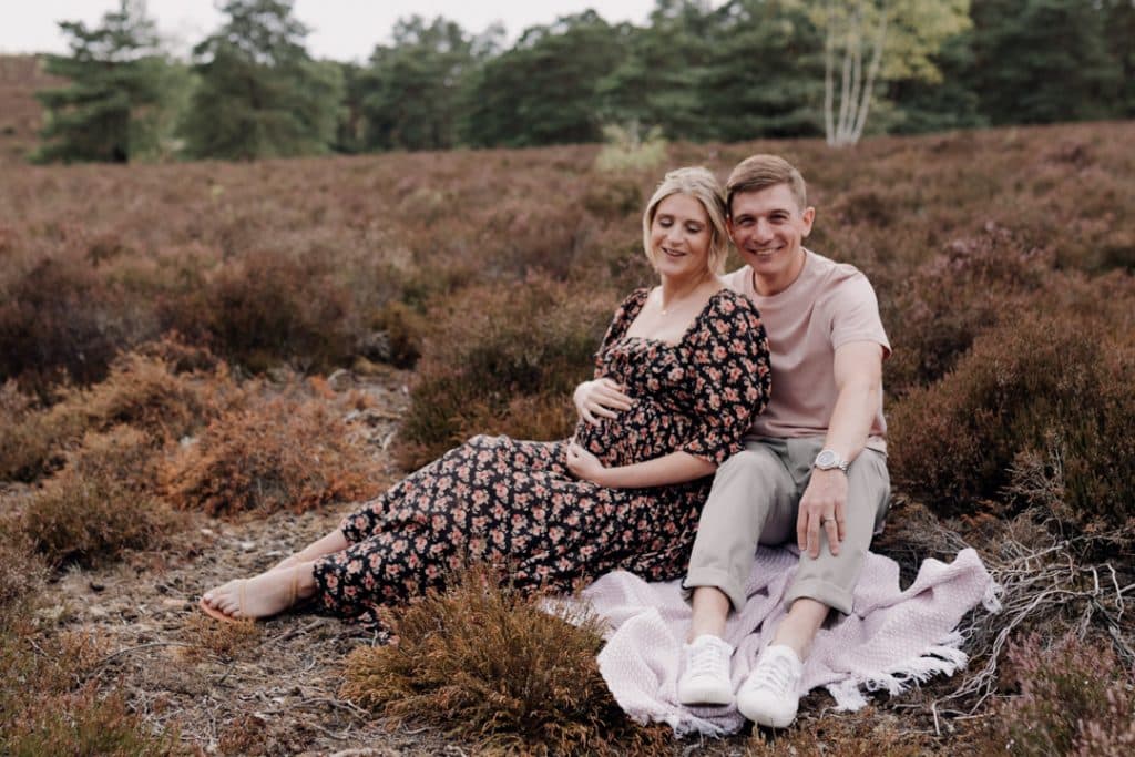 Expecting parents are sittin gon the blanket and smiling. Lovely natural sessings in the beautiful common. Hamphire family and matenrity photographer. Ewa Jones Photography