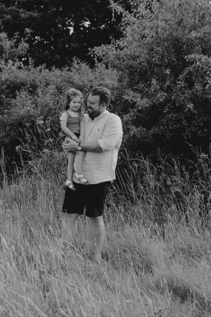 Dad is holing his daughter in his arms. He is looking at her and she is smiling. Lovely natural family photography. Basingstoke family phototographer. Ewa Jones Photography