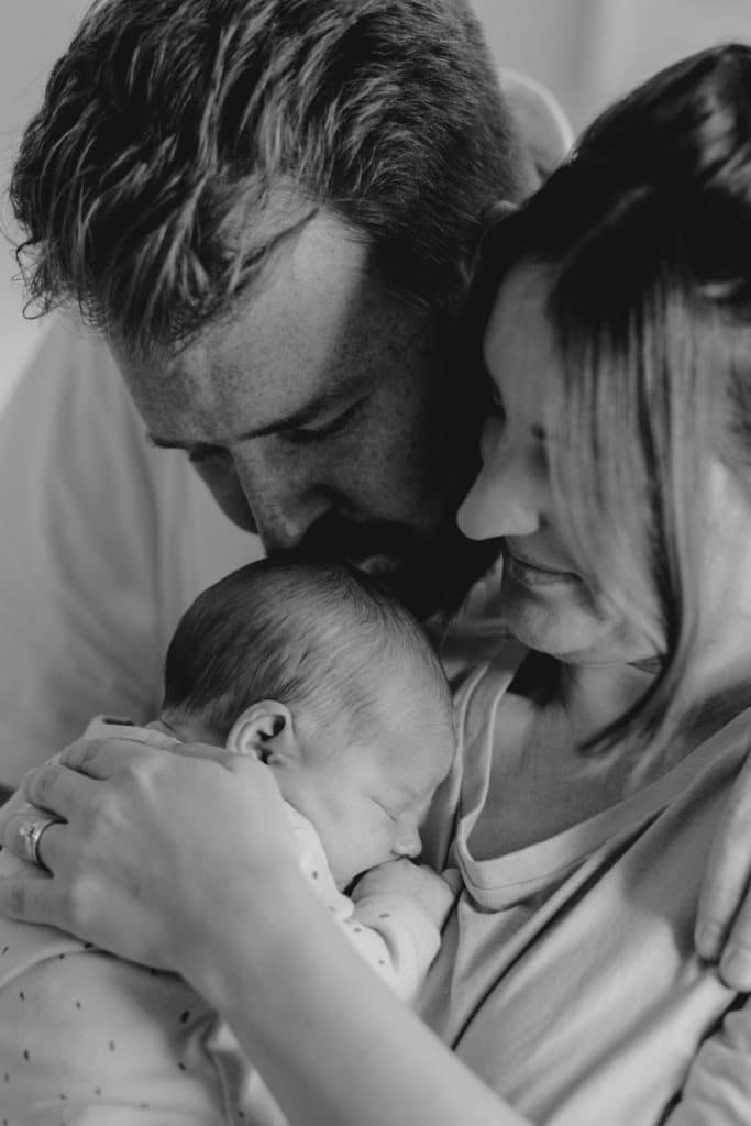 Mum and dad are hugging close their newborn baby girl. Newborn photography in Hampshire. Newborn photoshoot in Basingstoke. Ewa Jones Photography
