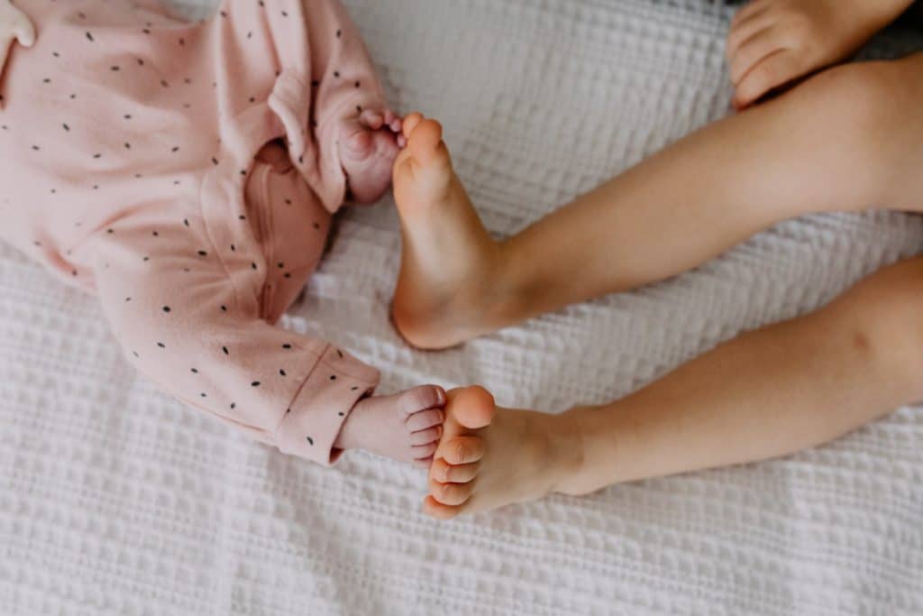 two sisters are measuring their feet. Newborn poses ideas with a sibling. Newborn photoshoot in Basingstoke. Ewa Jones Photography