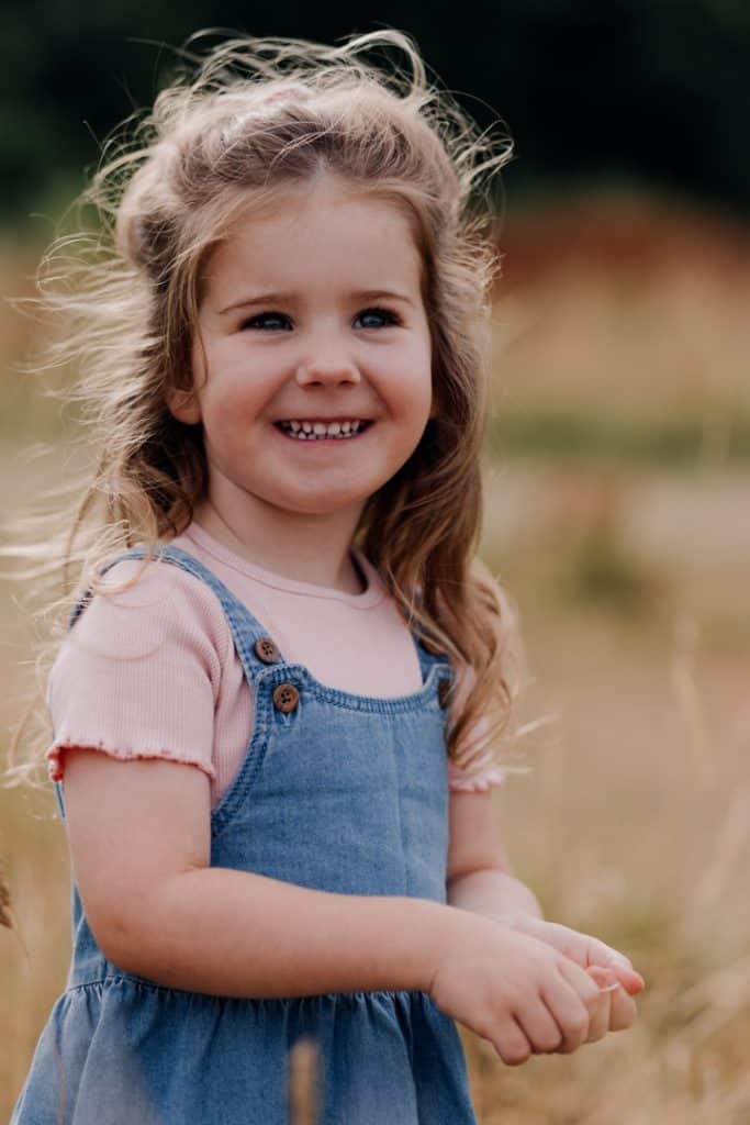Little girl is standing in the field and smiling. Natural family photo shoot in Basingstoke. Hampshire family photographer. Ewa Jones Photography
