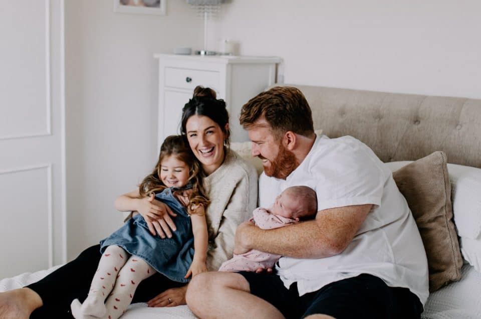 Family is sitting on the bed and laughing. Lovely natural lifestlye newborn photo shoot at home. Newborn photoshoot in Basingstoke. Ewa Jones Photography. Maternity and newborn photoshoot.