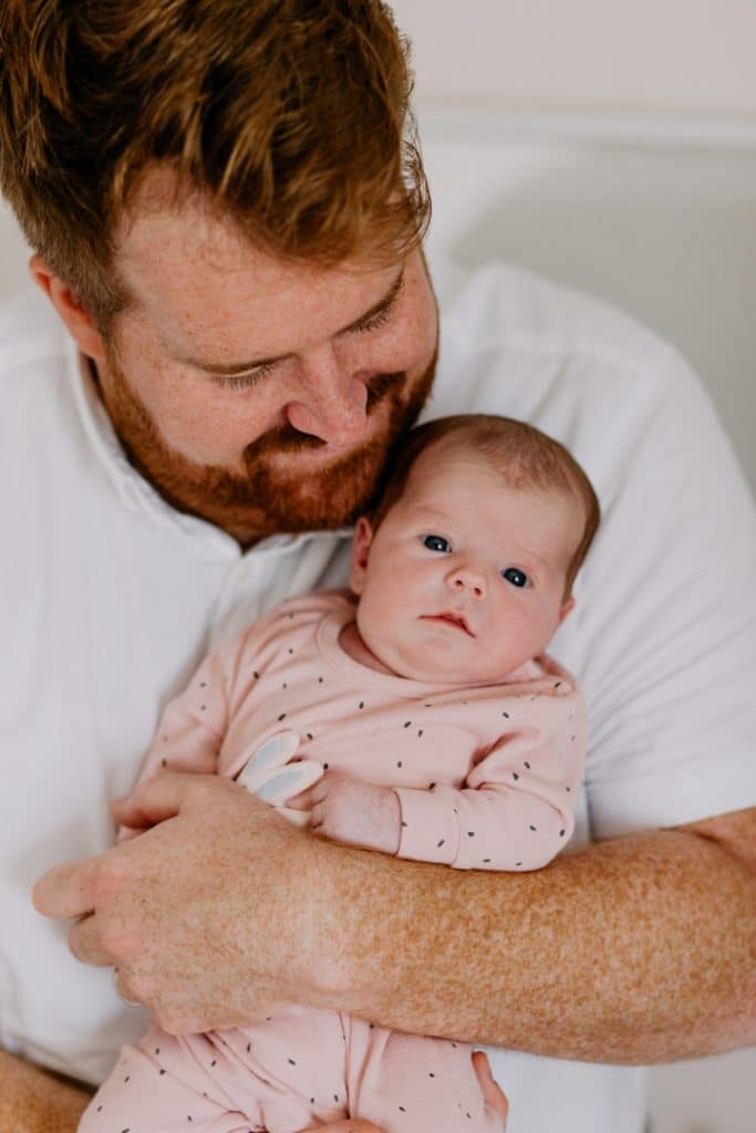 Dad is holding his newrborn baby girl. Baby girl is looking at the camera. Newborn photo shoot in Basingstoke. Ewa Jones Photography