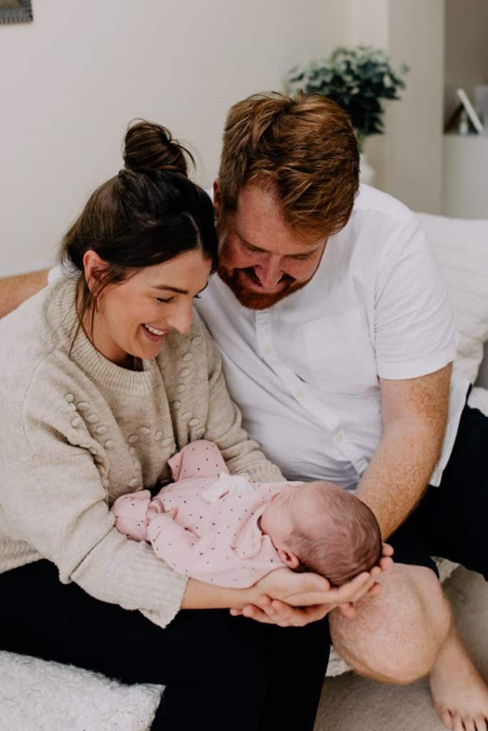 Mum and dad are holding baby girl and looking down at her. Newborn poses ideas. In home newborn photoshoot. Newborn photoshoot in Basingstoke. Ewa Jones Photography