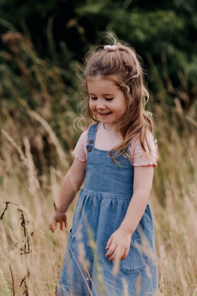 Little girl is standing in the long grass field smiling. natural lifestyle family photo session in hampshire. Basingstoke photographer. Ewa Jones Photography