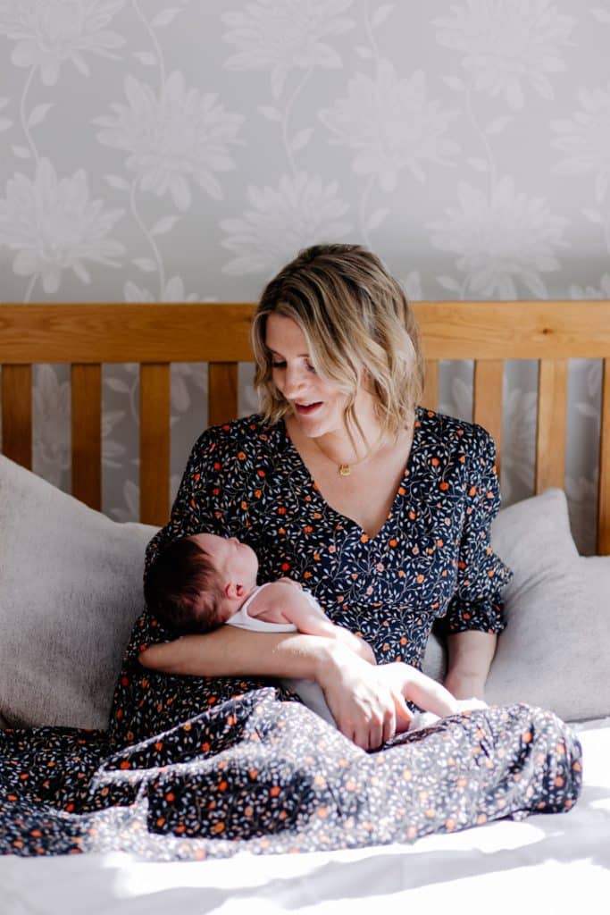 Mum is sitting on the bed and looking down at her baby girl. Lovely intimate newborn photo shoot at home. Newborn photographer in Hampshire. Ewa jones Photography
