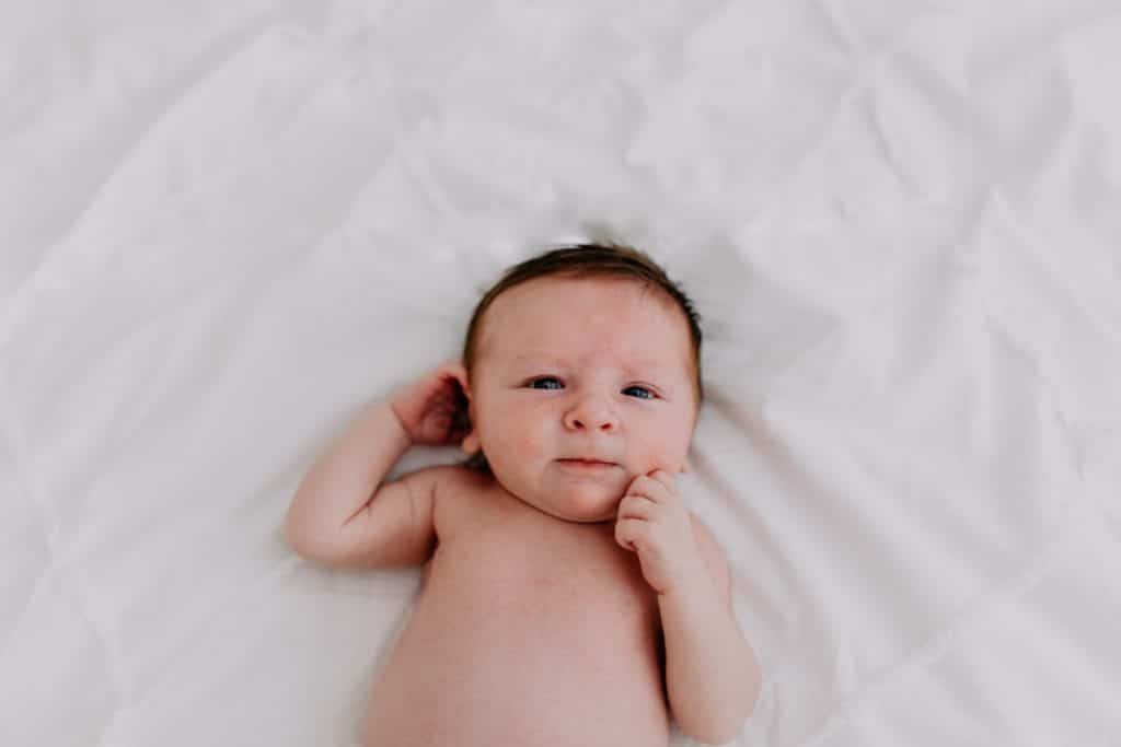 Newborn baby girl is laying on the bed and looking at the camera. Newborn photo shoot in Basingstoke Hampshire. Ewa Jones Photography