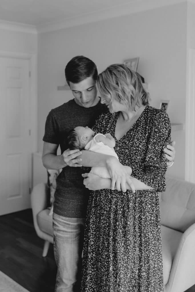 black and white image of parents cuddling and looking at their baby girl. Lifestyle in home newborn photo session in Basigstoke Hampshire. Ewa Jones Photography