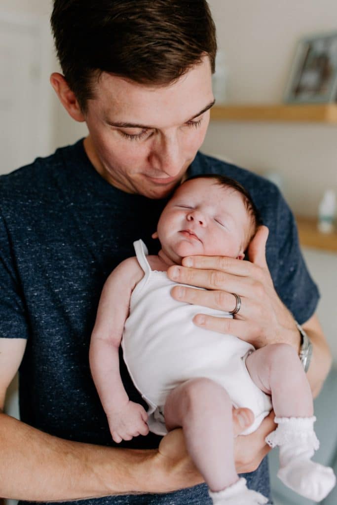 Dad is cuddling his baby girl and looking at her. baby girl is sleeping. Newborn baby photo session in Basingstoke Hampshire. Ewa Jones Photography