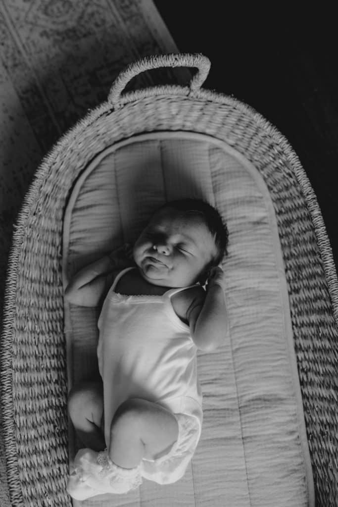 newborn baby girl is laying in her moses basket and stretching. lovely lifestlye photo. Newborn photo shoot in Basingstoke Hampshire. Ewa Jones Photography