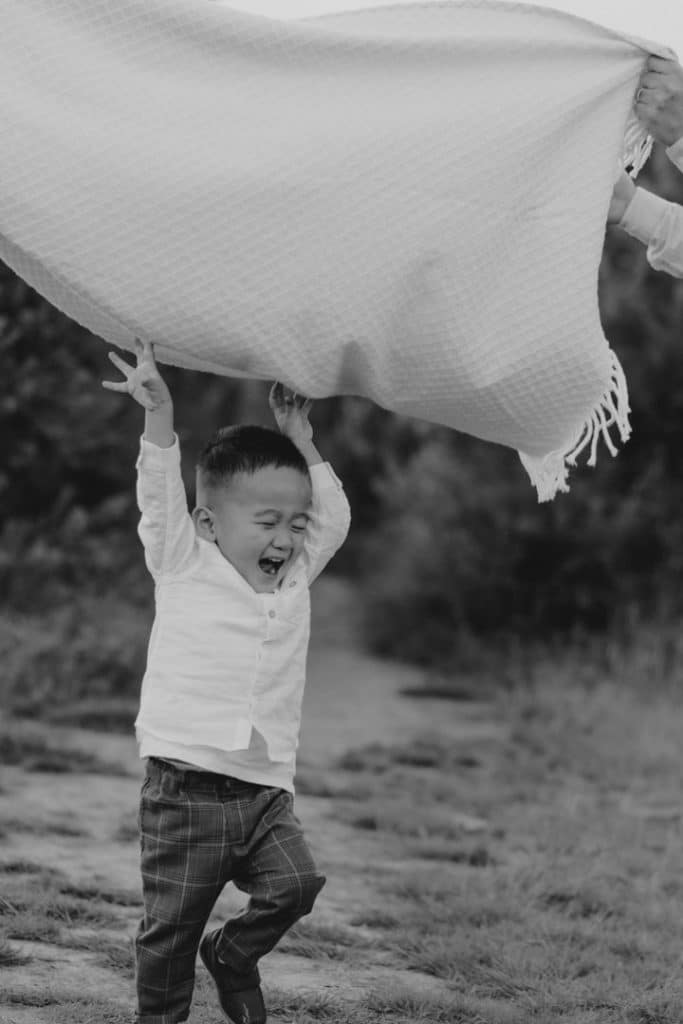 Little boy is running through the blanket and has his hands up in the air. Natural lifestyle family photo shoot in Surrey. Lifestyle family photo session. Ewa Jones Photography