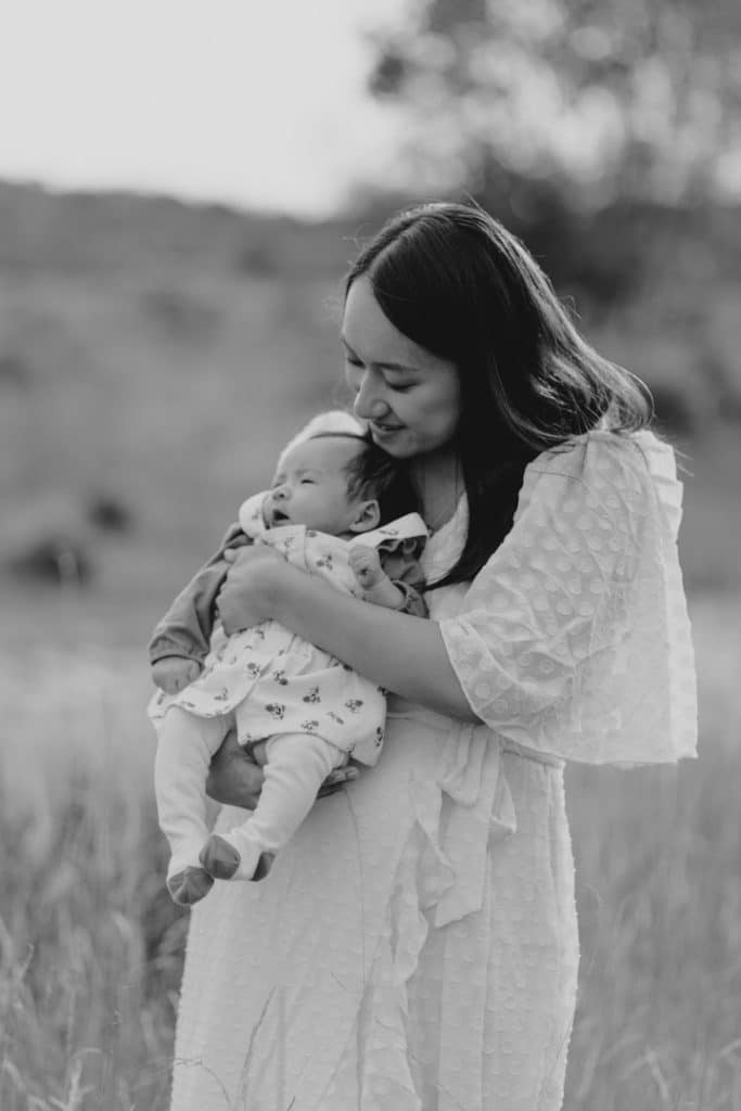 Mum is holding her little baby girl and looking down on her. Baby photo session outside. Black and white photography. Family photography in Surrey. Ewa Jones Photography