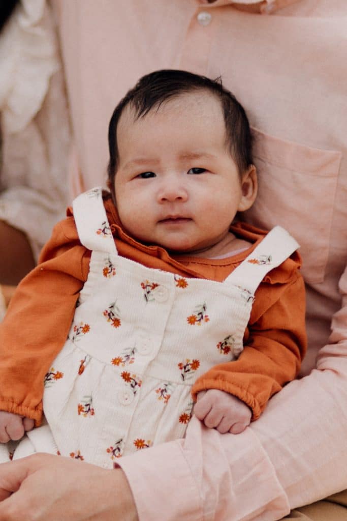 Little baby girl is being held by dad and she is looking at the camera. Lovely family photoshoot in Surrey. Hampshire photographer. Ewa Jones Photography