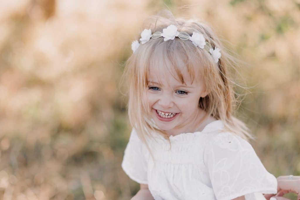 Little girl is smiling. she is wearing lovely white dress. family photo shoot in Basingstoke. Hampshire photographer. Ewa jones photography