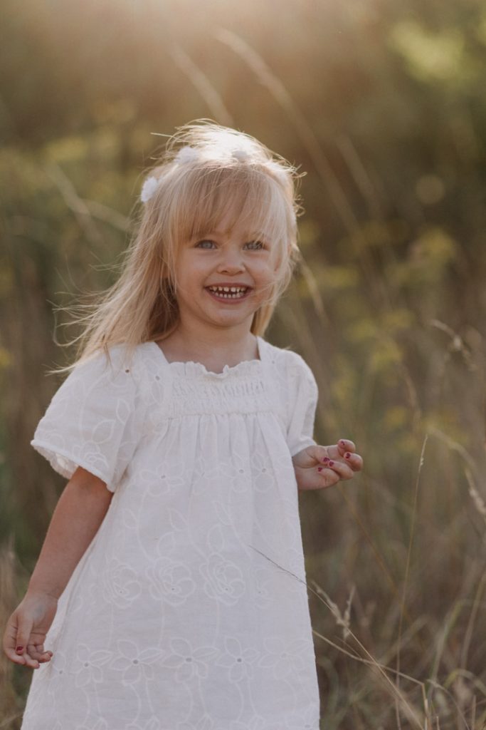 Little girl is standing in the field and smiling. family photo shoot in Basingstoke Hampshire. Hampshire family photographer. Ewa Jones Photography