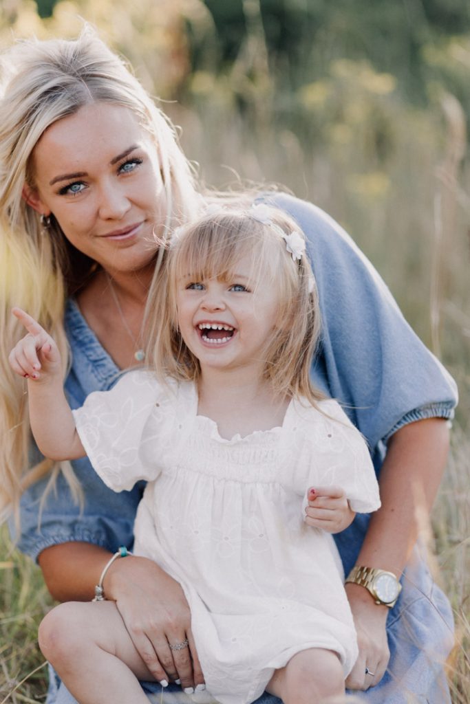 mum and her daughter are sitting on the field and smiling. family photo session. lifestyle family photo shoot in Basingstoke. Hampshire family photographer. Ewa Jones Photography