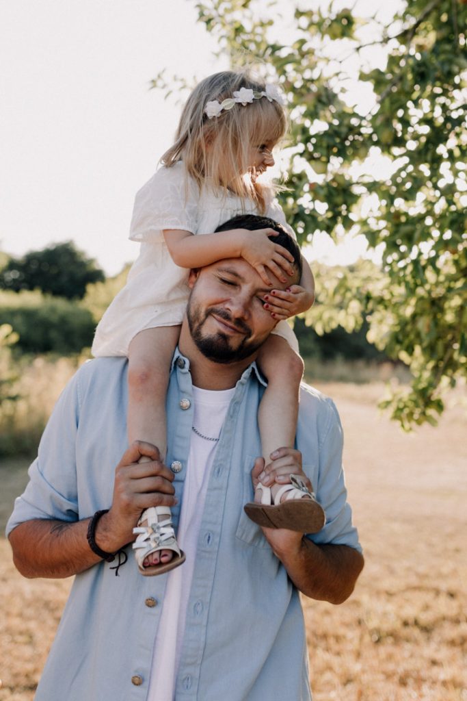 little girl is on daddy's shoulders and she is laughing and daddy is smiling too. cute family photo shoot in Hampshire. Hampshire family photographer. Ewa Jones Photography