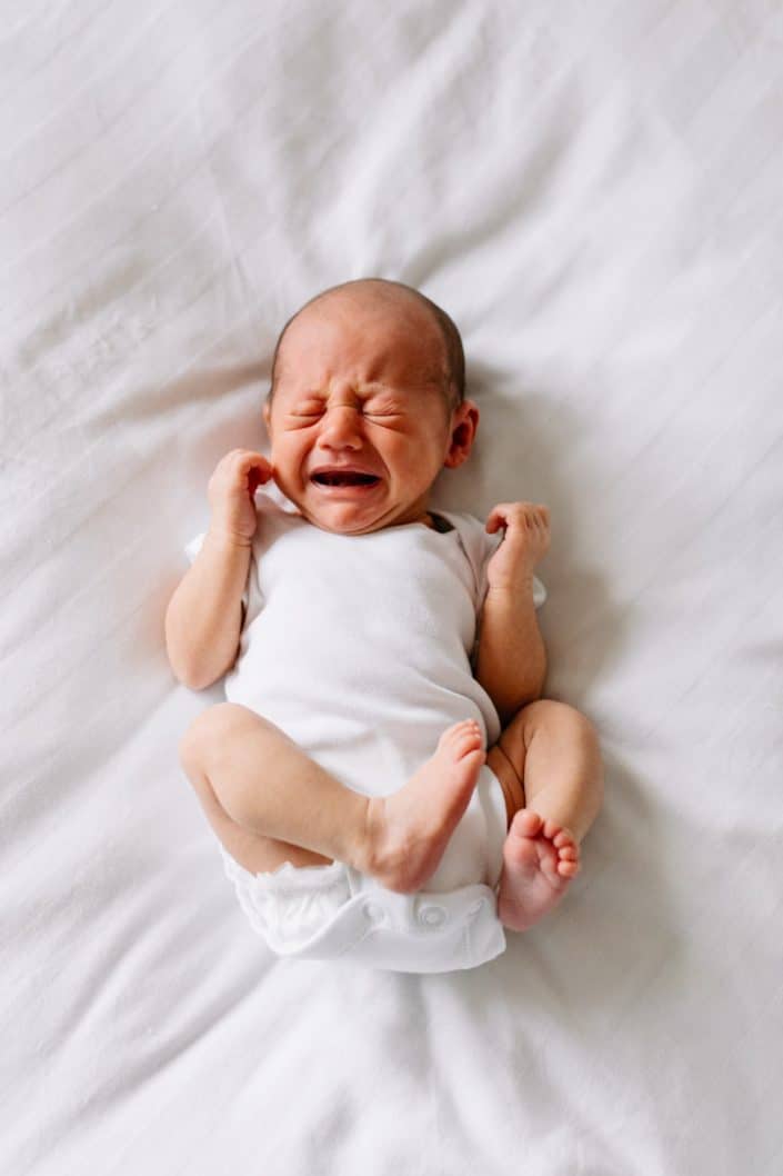 Newborn baby is crying and laying on the bed. lifestyle newborn photo shoot at home. Newborn photographer in Hampshire. Ewa Jones Photography