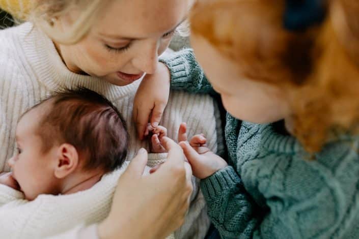 Newborn baby is laying on mummy and her older sister is counting her fingers. Newborn photography in Hampshire. Basingstoke photographer. Ewa Jones Photography