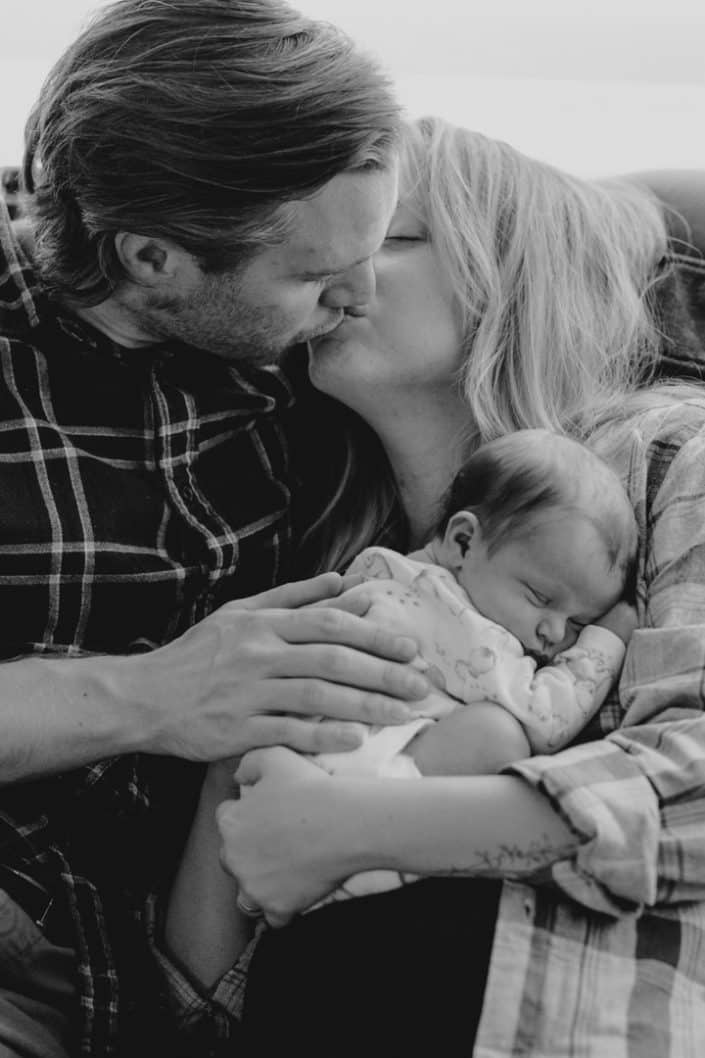 Mum and dad are kissing and holding their baby girl. Newborn photo shoot in Hampshire. Newborn photographer. Ewa Jones Photography