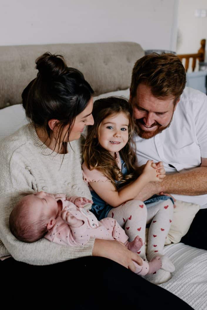 Family of four is cuddling on bed. mum is holding newborn baby girl. Newborn photography in Hampshire. Basingstoke newborn photographer. Ewa Jones Photography