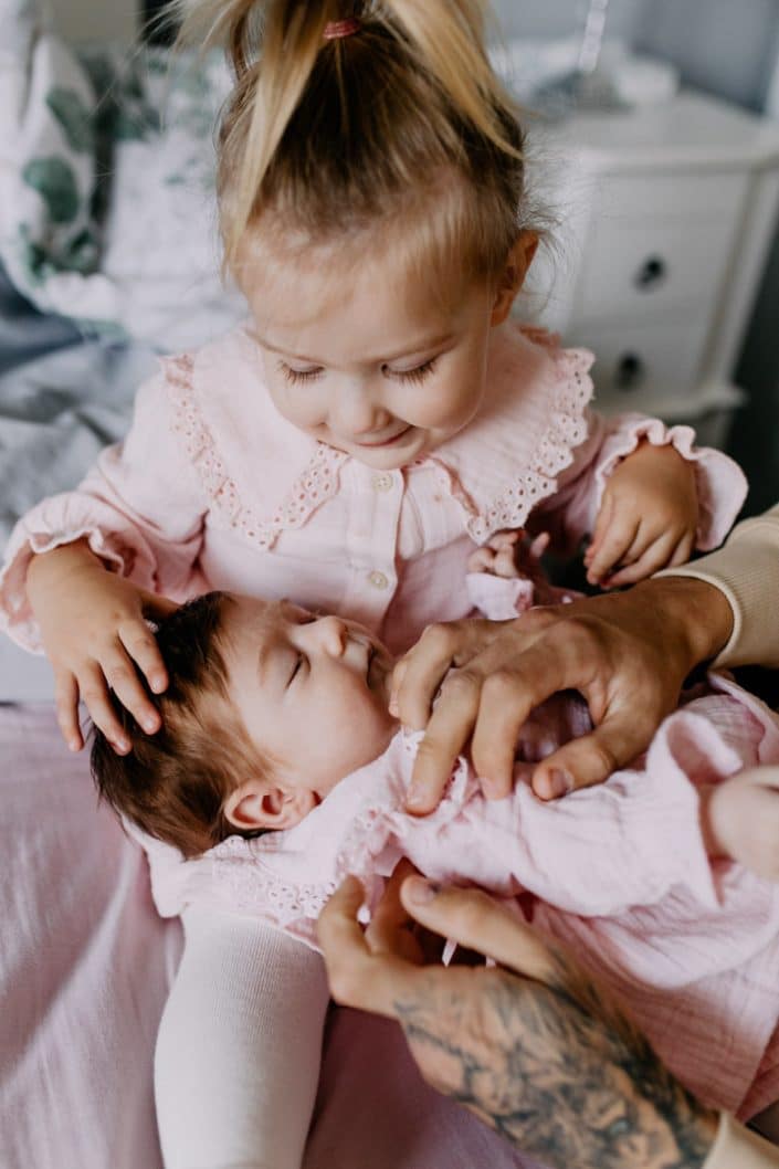 Newborn baby girl is laying and sleeping and her sister is cuddling her. Lovely image of two sisters. Newborn baby photo shoot in Hampshire. Newborn photography Hampshire. Ewa Jones Photography