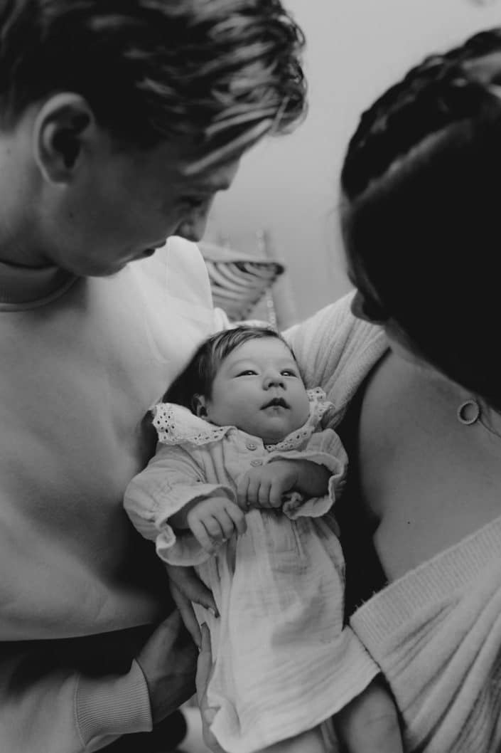 Mum and dad are holding their newborn girl and looking down on her. Candid newborn photoshoot. Hampshire photographer. Newborn photo session in Hampshire. Newborn baby girl is laying and sleeping and her sister is cuddling her. Lovely image of two sisters. Newborn baby photo shoot in Hampshire. Newborn photography Hampshire. Ewa Jones Photography