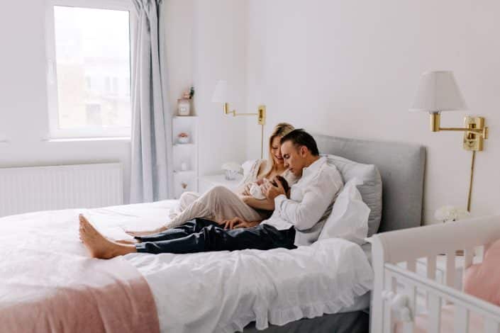 Mum and dad are sitting on the bed and looking down at their baby girl. Newborn phototoshoot in London. Hampshire newborn photography. Ewa Jones Photography