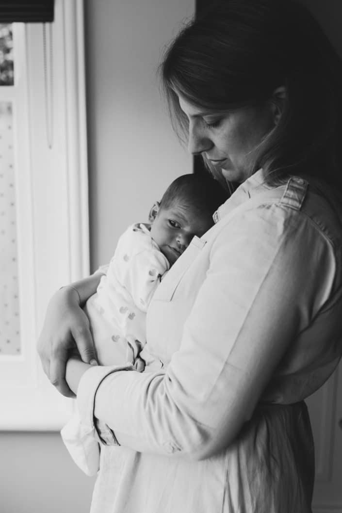 mum is cuddling her newborn baby and looking down on him. lifestyle in home newborn photo session. Newborn photography in Hampshire. Ewa Jones Photography