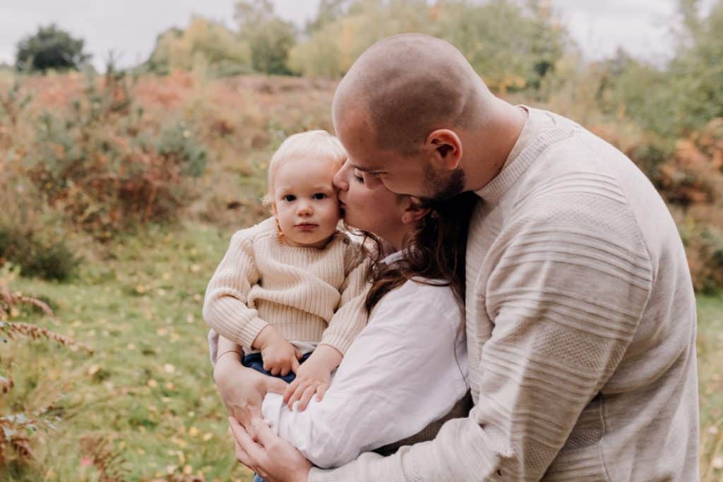Mum and dad are cuddling their baby boy close. they are wearing lovely autumn clothes. Basingstoke family photographer. Hampshire photo shoot. Ewa Jones Photography