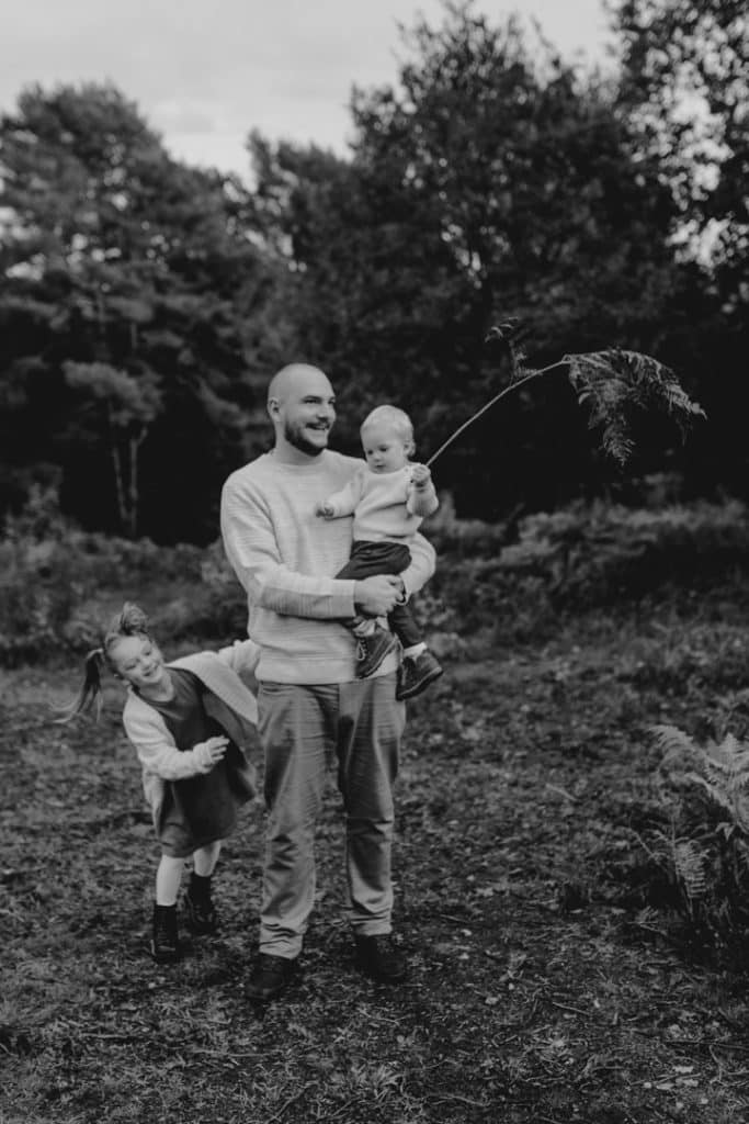 Dad is holding son in his arms and little girl is behind his legs. fun and natural family photo session in Hampshire. Basingstoke family photographer. Ewa Jones Photography