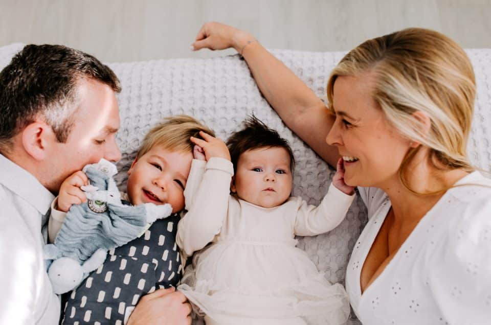 family of four is laying on the bed and smiling. newborn photo session in Hampshire. lifestyle photographer in Hampshire. Ewa Jones Photography. Newborn photo session through a client referral