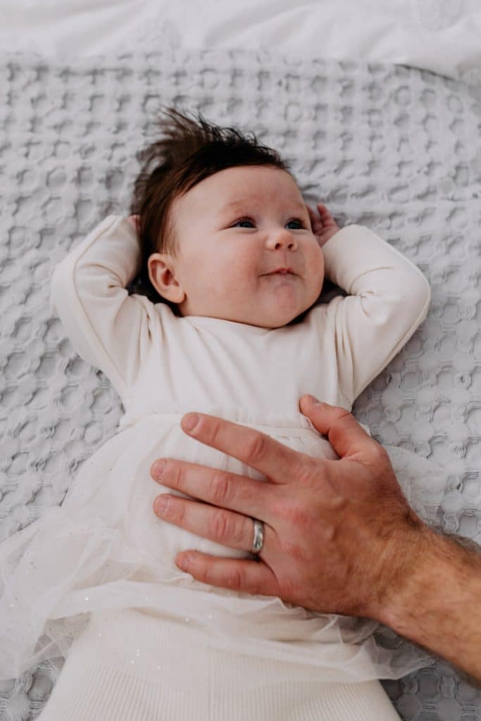 Newborn baby girl is laying on bed and looking at dad. Dad is holding his hand on her tummy. lovely candid natural photo shoot. Hampshire photographer. Ewa Jones Photography