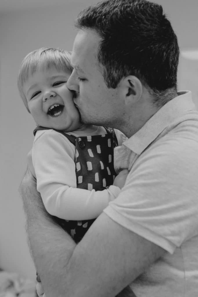 Dad is cuddling and kissing his boy and he is laughing. family photographer in hampshire. Ewa Jones Photography.