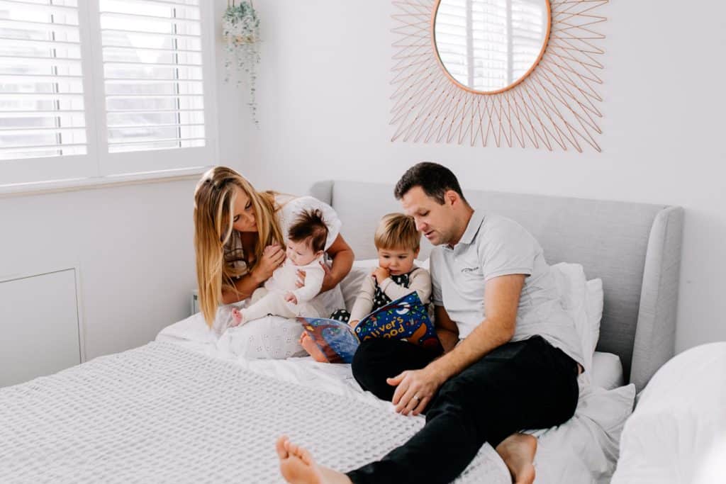 family of four are sitting on the bed and enjoying reading a story. Hampshire newborn photo session with older sibling. Hampshire photographer. Ewa Jones Photography.