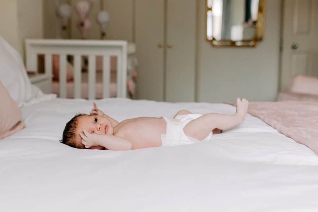 Newborn photo shoot in London-1 Newborn baby girl is laying on bed. She is wearing a nappy and her baby nursery is white and pink. newborn photo session. Hampshire newborn photographer. Ewa Jones Photography