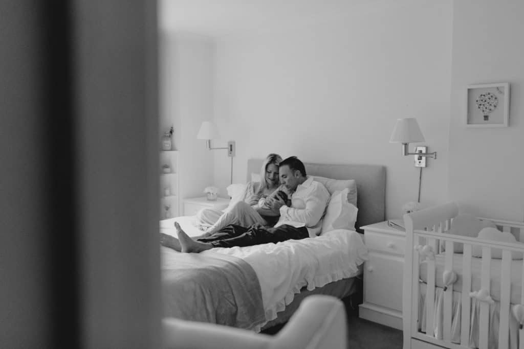 Newborn photo shoot in London-13 Mum and dad are sitting on the bed and cuddling their newborn girl. Lovely photograph of this special moment. Newborn photo shoot in London. Hampshire newborn photographer. baby photo session. Ewa Jones Photography