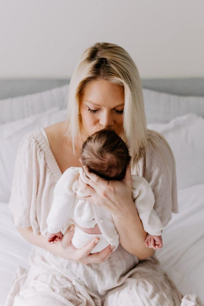 Newborn photo shoot in London-18 Mum is kissing her newborn baby girl and sitting on the bed. London newborn baby photo session. Hampshire newborn photographer. Basingstoke newborn baby photo shoot. Ewa Jones Photography